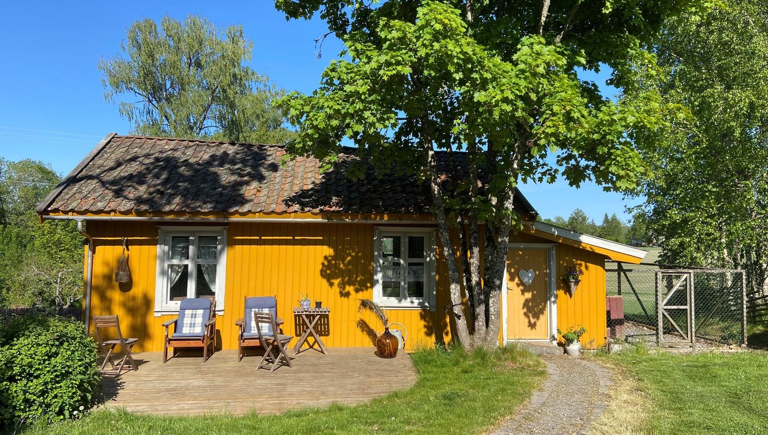 Den gule Veslestua sett utenifra med solstoler og hundegård