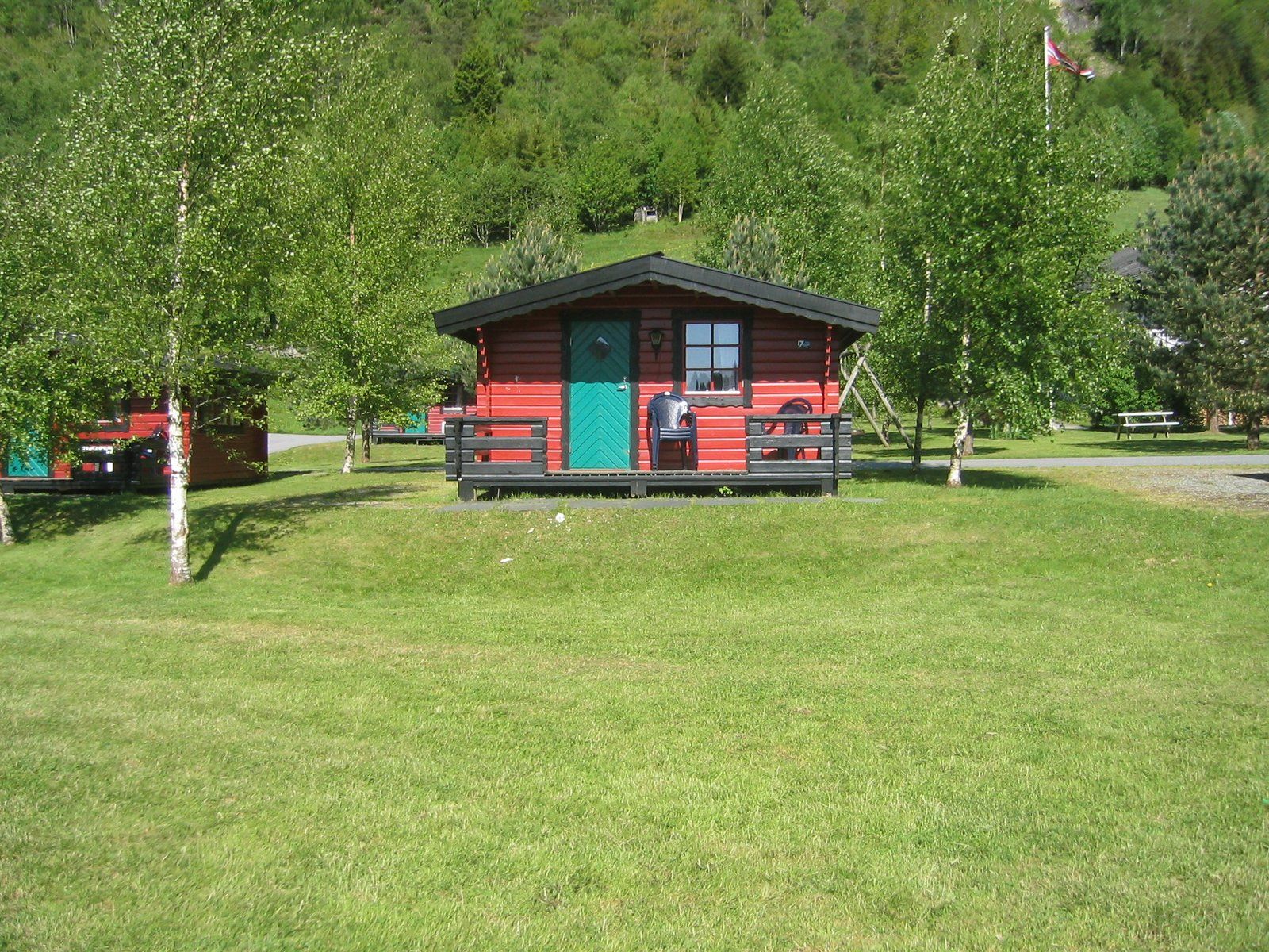 Red camping cabin surrounded by birch trees and green meadows at Folgefonn Cabins and Farm Camping.

