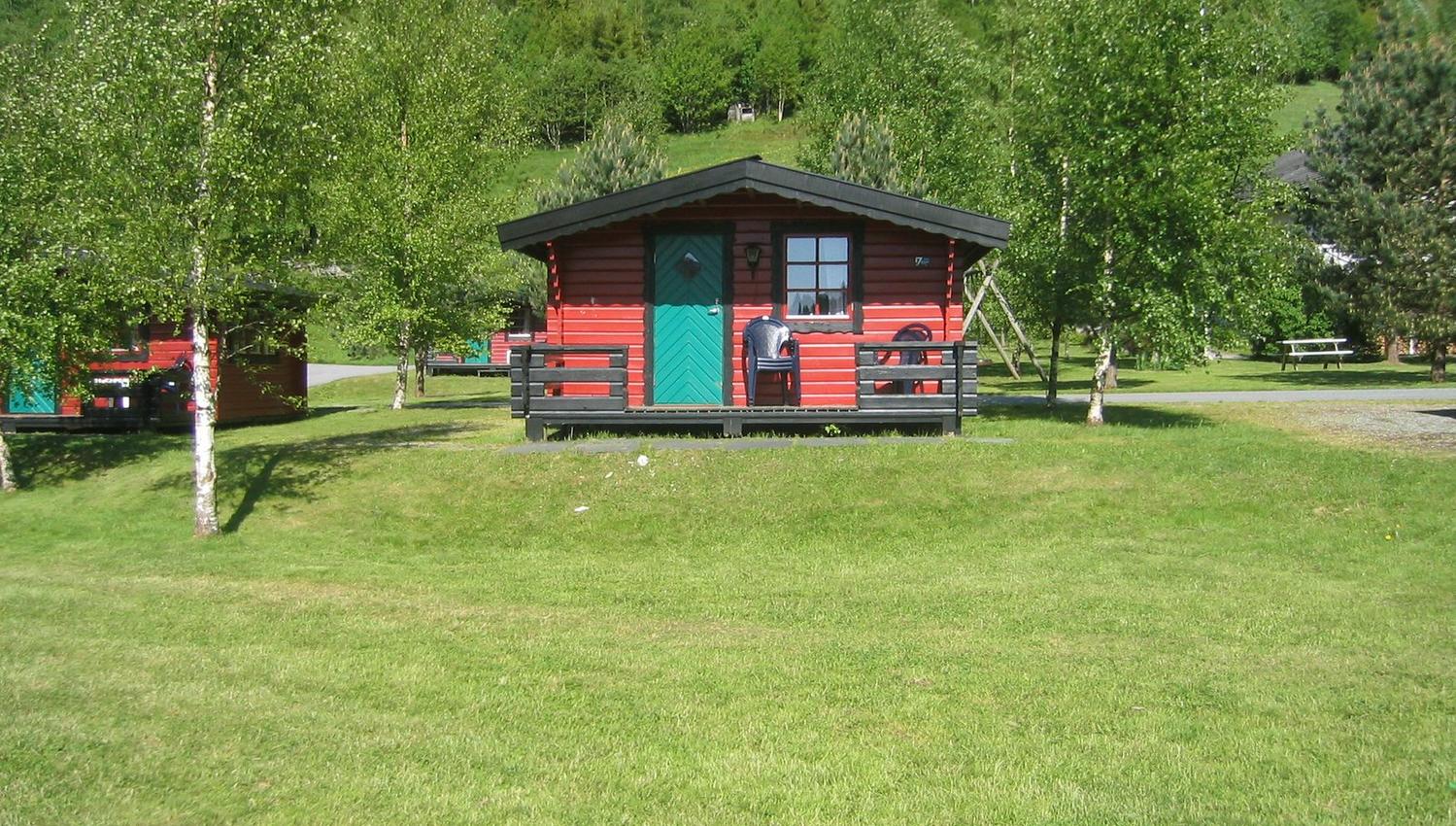 Red camping cabin surrounded by birch trees and green meadows at Folgefonn Cabins and Farm Camping.