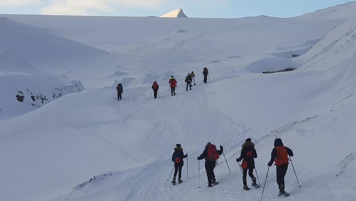 To grupper med gjester på fottur i snødekte omgivelser på vei opp en fjellside