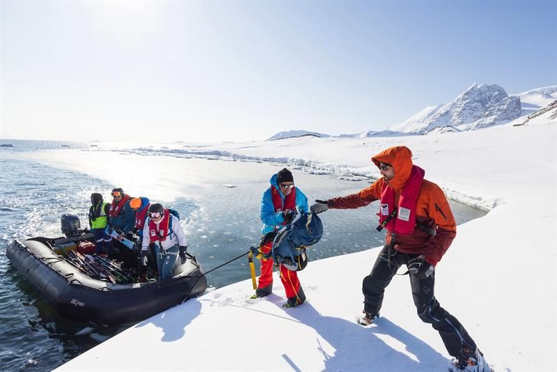 En gummibåt legger i land i vinterlandskap. Båten har mennersker og ski i seg.