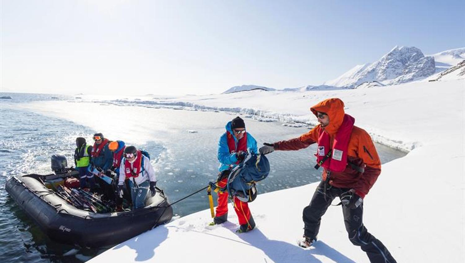 En gummibåt legger i land i vinterlandskap. Båten har mennersker og ski i seg.