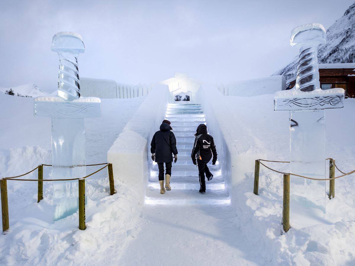 Gjester går opp den belyste trappen til Tromsø Ice Domes. Den er laget av is og snø.