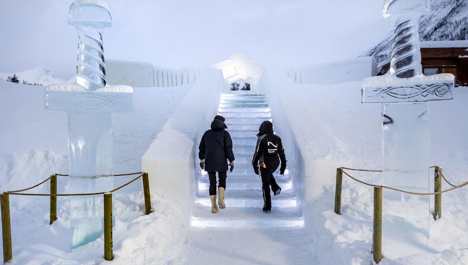 Gjester går opp den belyste trappen til Tromsø Ice Domes. Den er laget av is og snø.
