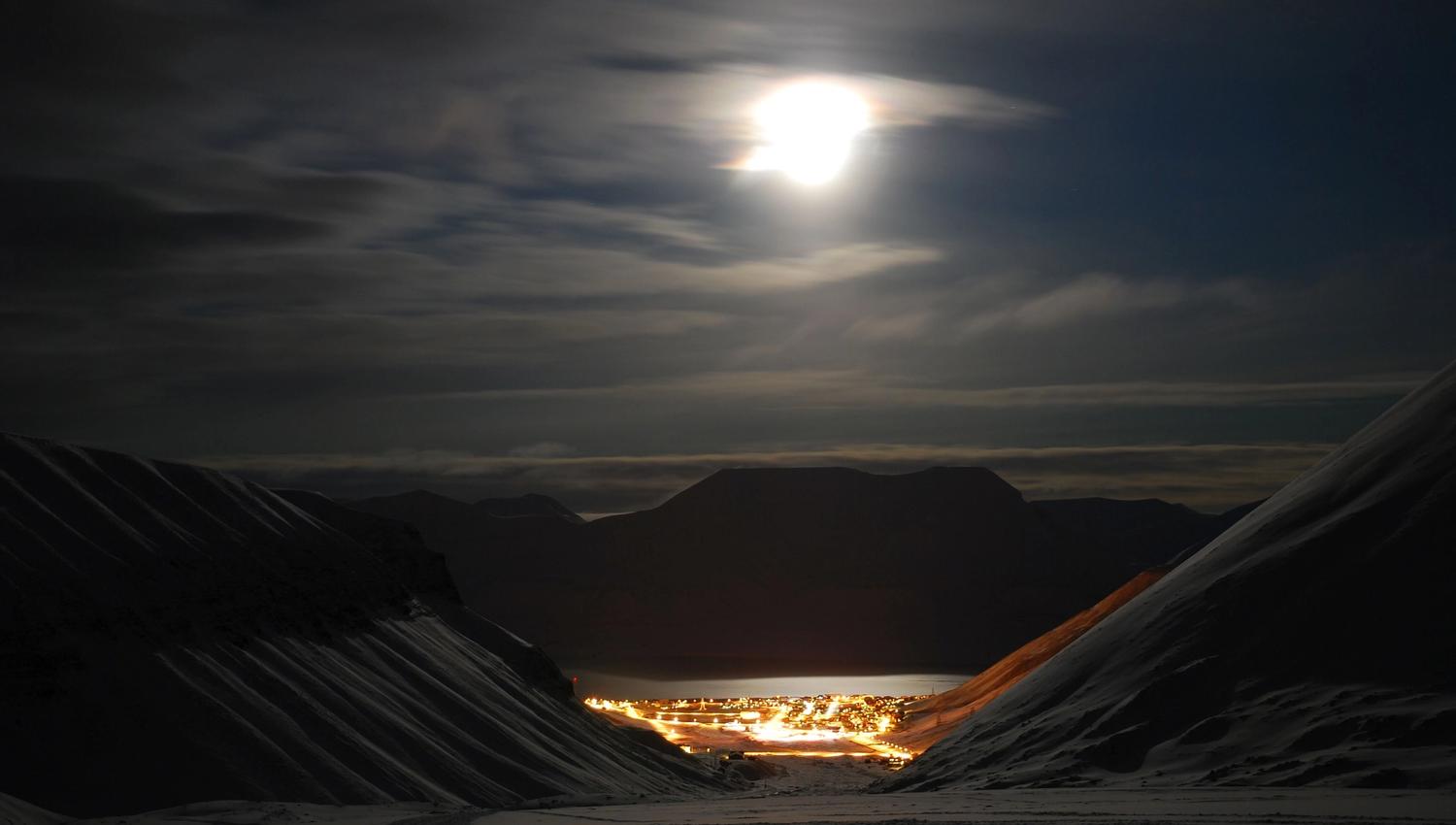 Longyearbyen i enden av dalen. Måneskinnet lyser opp fjellene rundt.