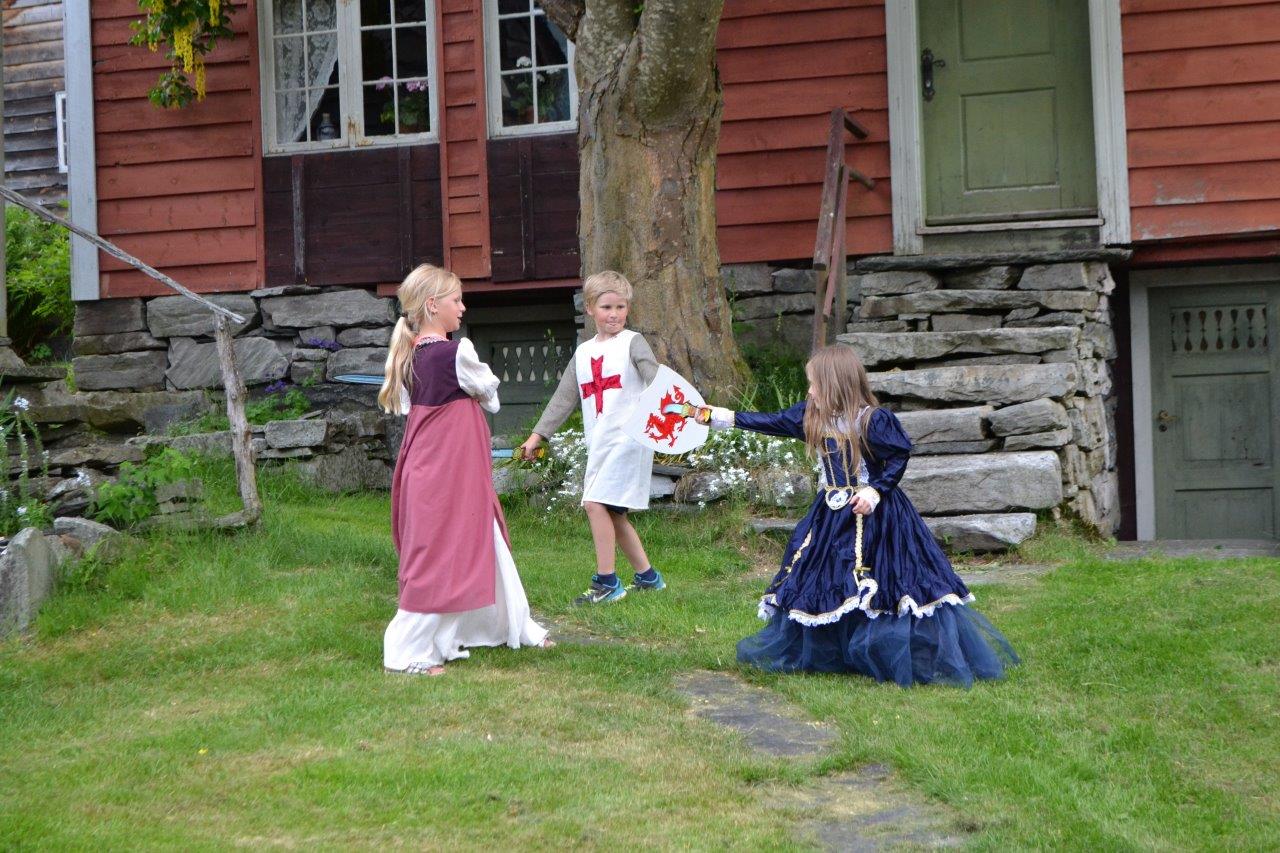 Three kids dressed up in medieval costumes playing in the garden. 