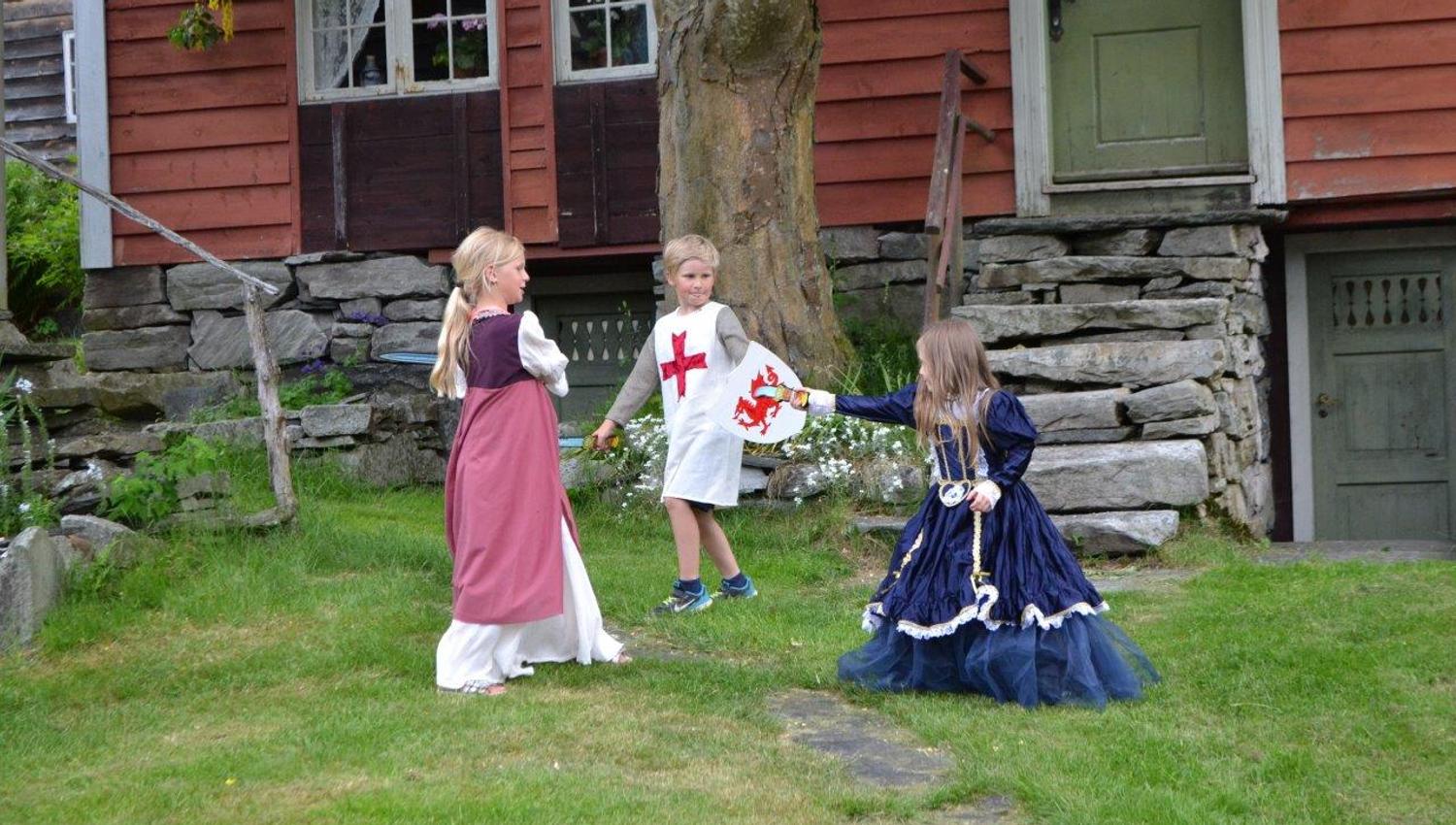 Three kids dressed up in medieval costumes playing in the garden.