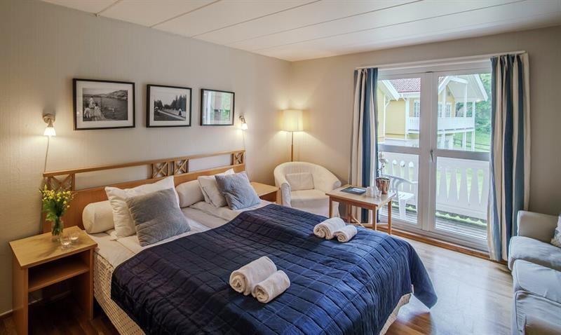 Lyst hotellrom på Hankø Hotell & Spa, med dobbeltseng, blått sengeteppe, sittegruppe og balkongdør med utsikt mot hagen.