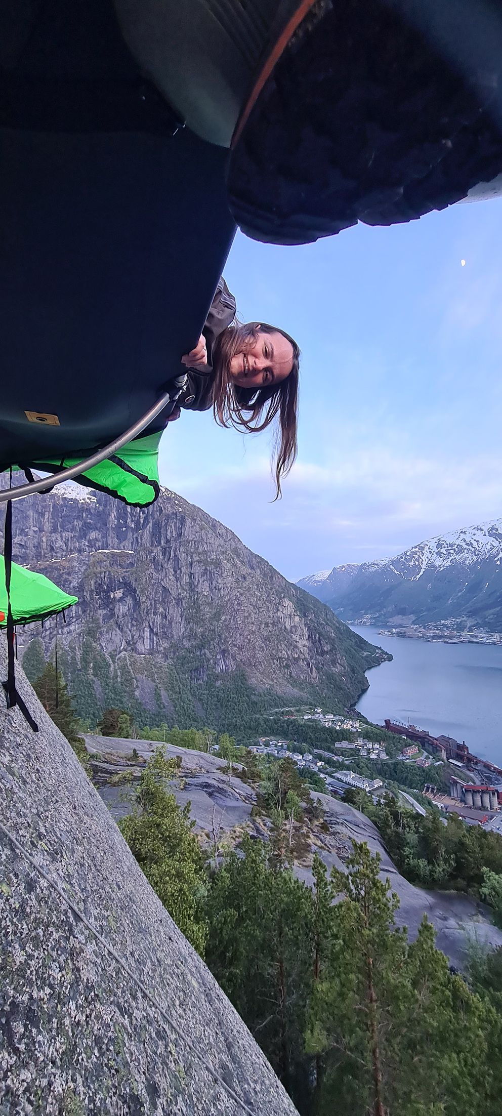 Ei kvinne smilar og stikk hovudet ut frå ein portaledge, med fjorden langt under ho i Hardanger. Eit eventyrleg overnattingsalternativ.