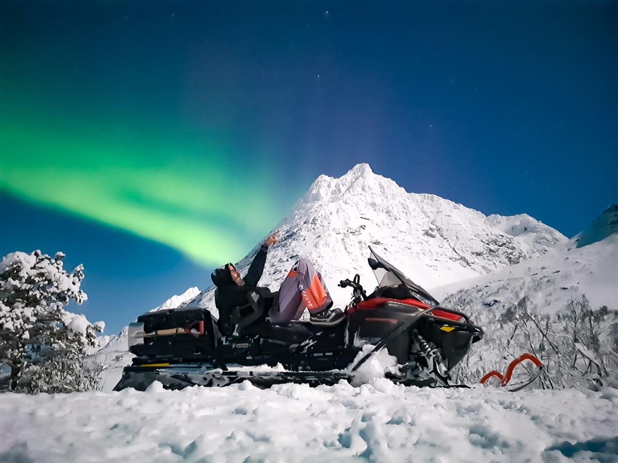 En person på snøskuter som ser opp på nordlyset