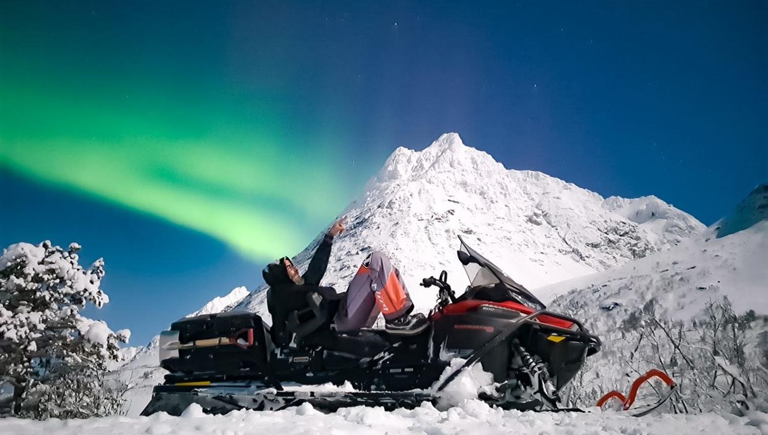 En person på snøskuter som ser opp på nordlyset