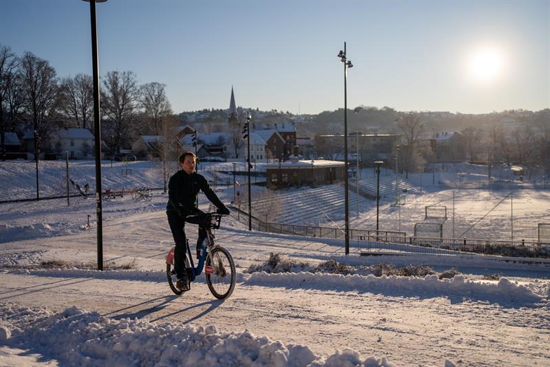 Mann som sykler på en snødekt vei, med en fotballbane i bakgrunnen