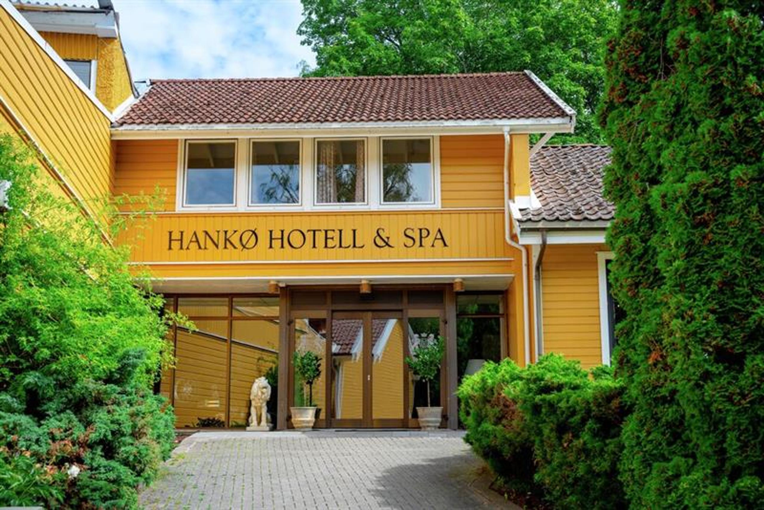 Hovedinngangen til Hankø Hotell & Spa, en gul trebygning omgitt av grønne trær og busker.