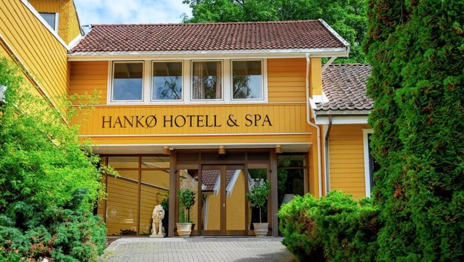 Hovedinngangen til Hankø Hotell & Spa, en gul trebygning omgitt av grønne trær og busker.