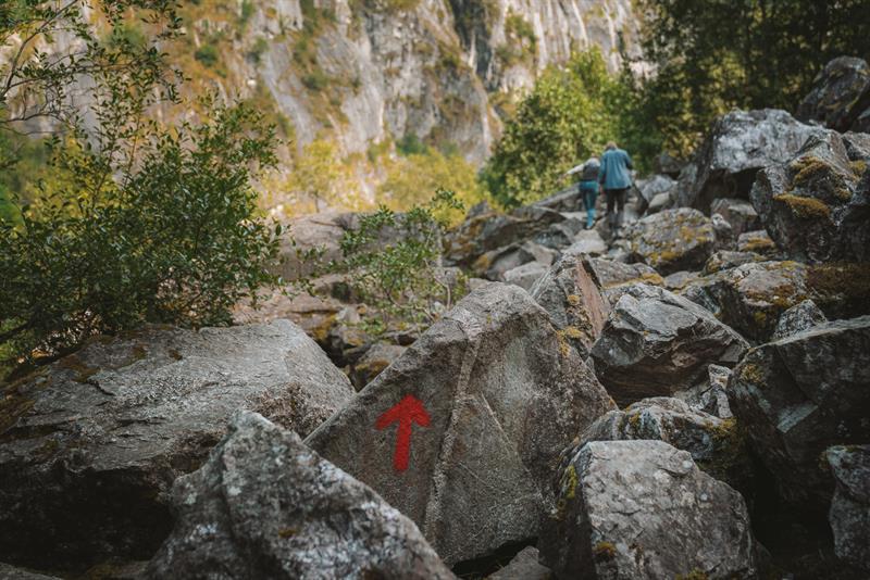 A large rock painted with a red arrow with a couple of hikers seen far in the background.