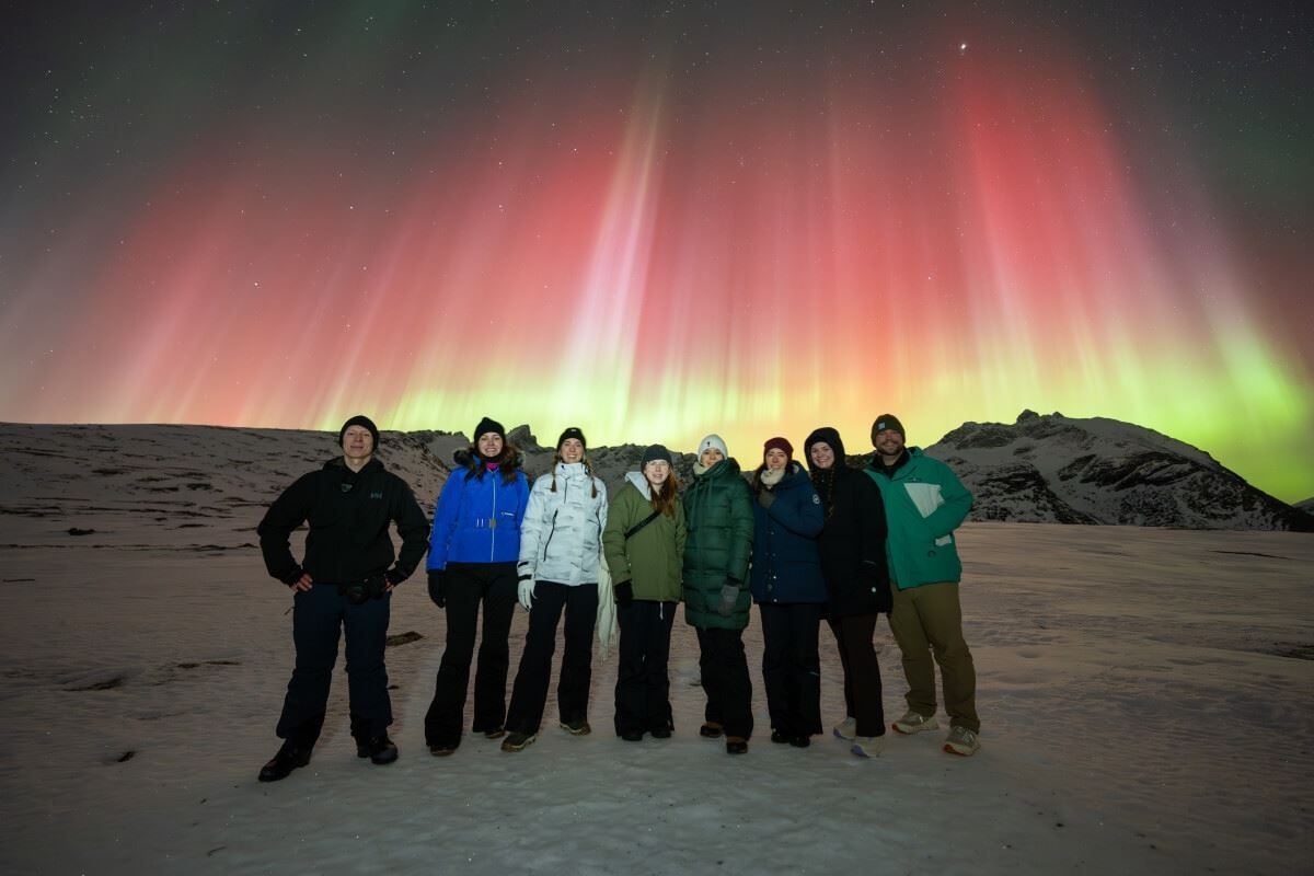A group of guests pose in front of red and green Northern Lights
