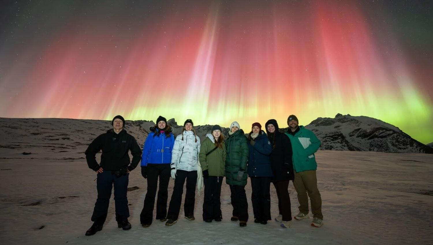 A group of guests pose in front of red and green Northern Lights