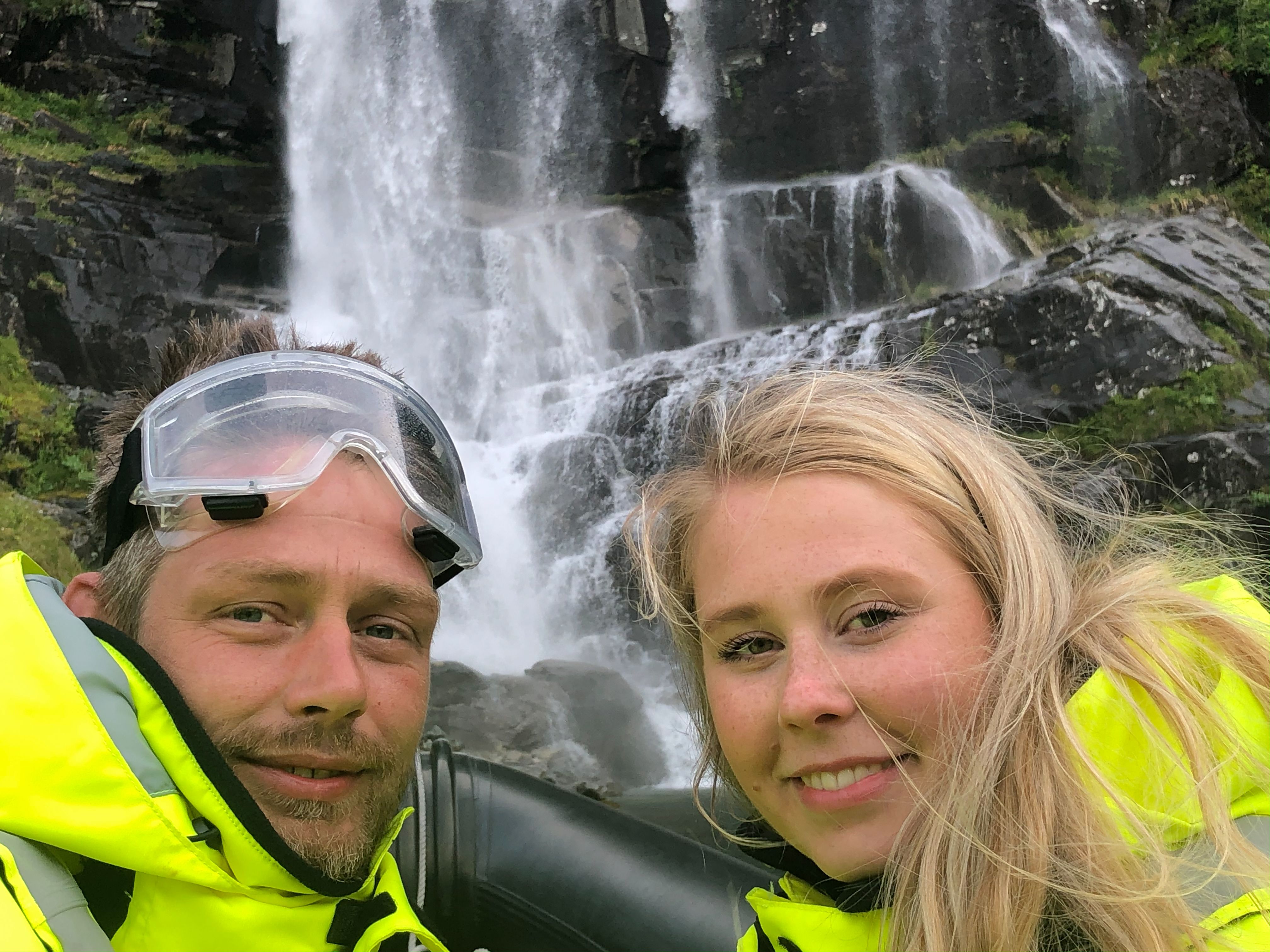 Two smiling adventurers take a selfie in front of a stunning waterfall in Hardanger.