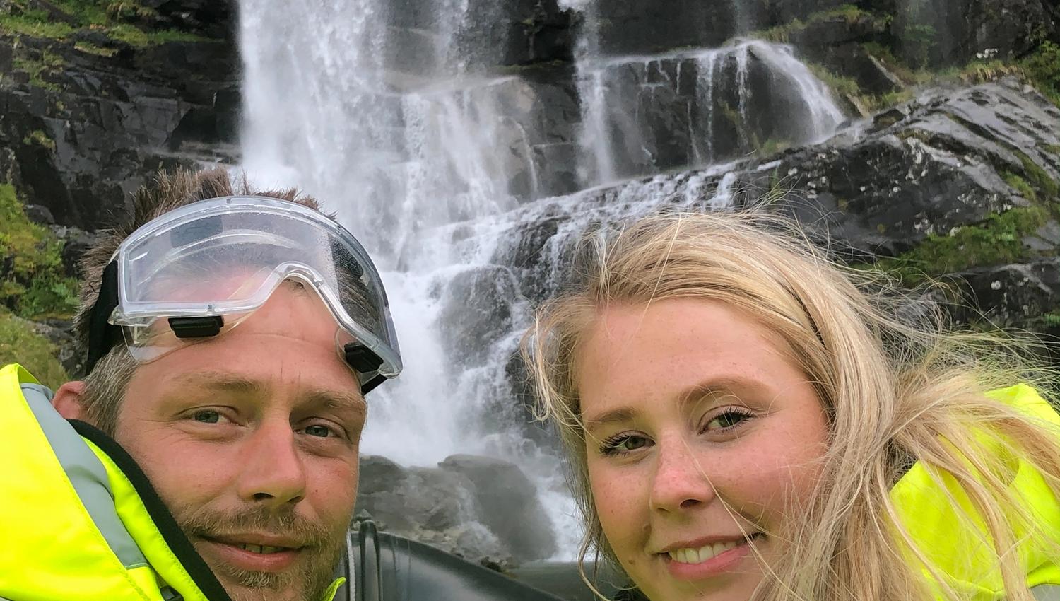 Two smiling adventurers take a selfie in front of a stunning waterfall in Hardanger.