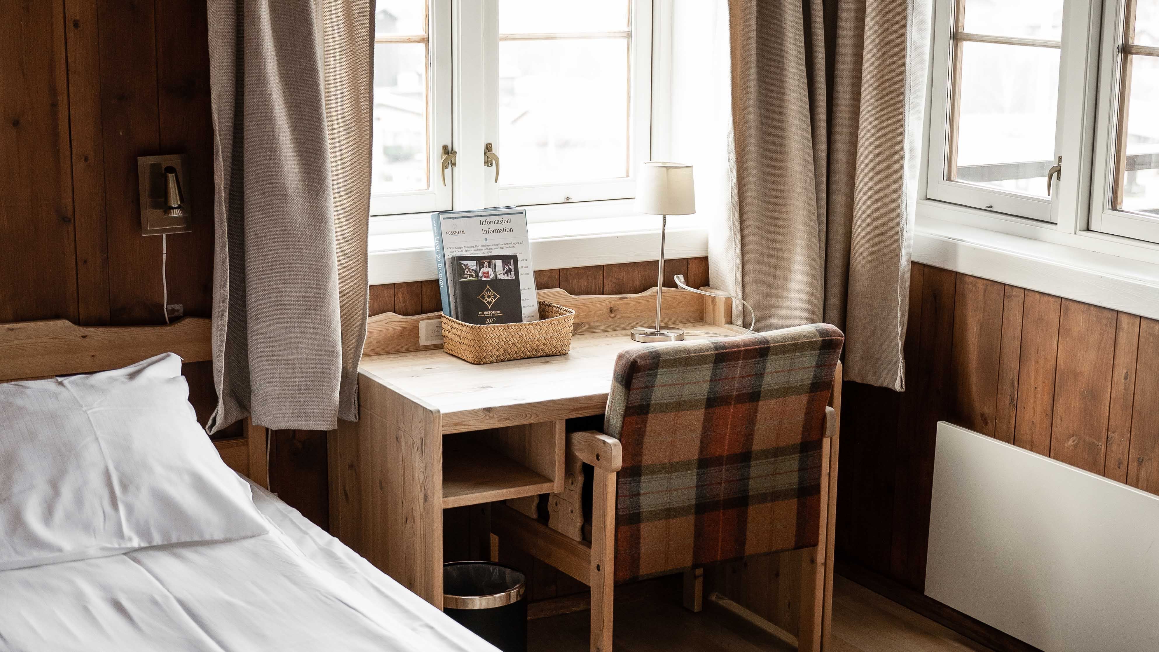 Houten kamer met een klein bureau met heldere ramen, grijze gordijnen, tafellamp, mand met papieren en geruite stoel...
