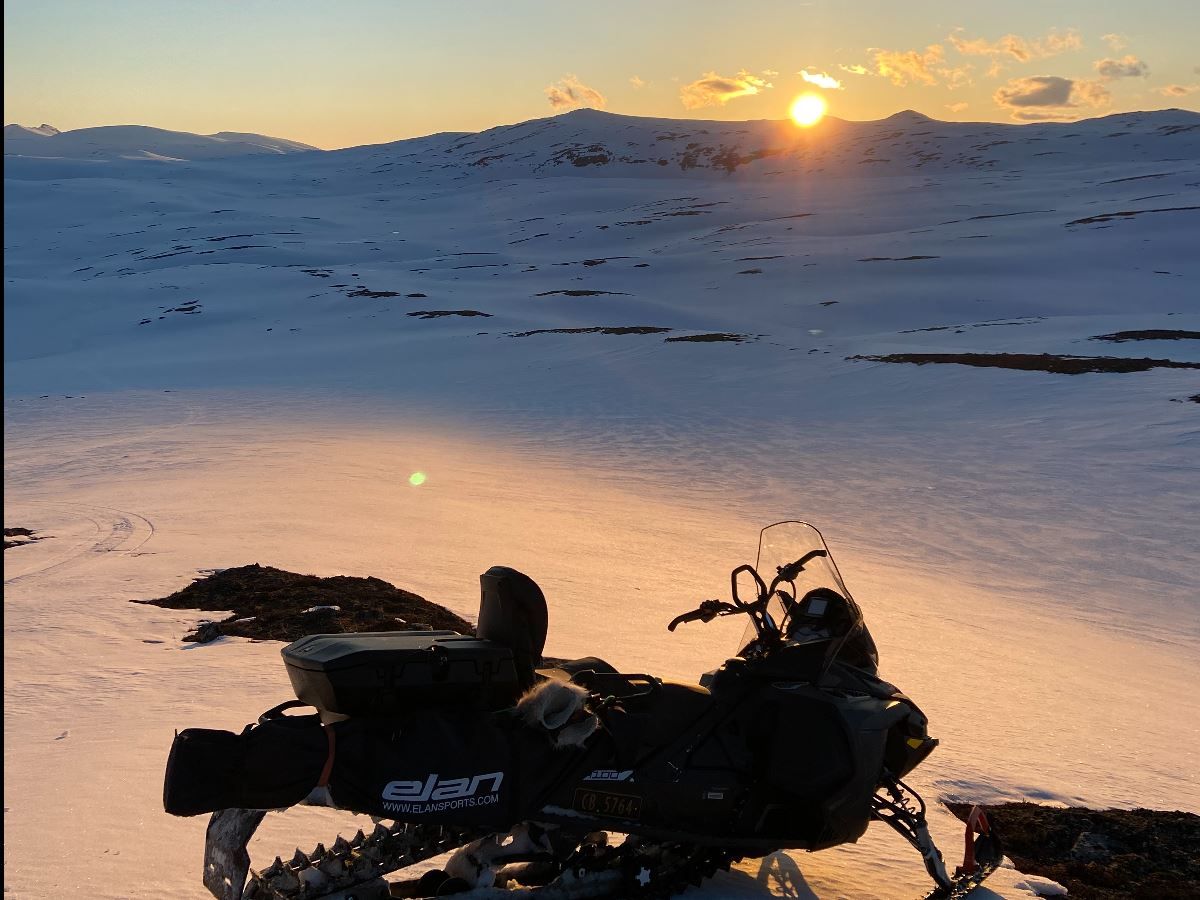 A snowmobile on the mountain with the sun just rising above the peaks