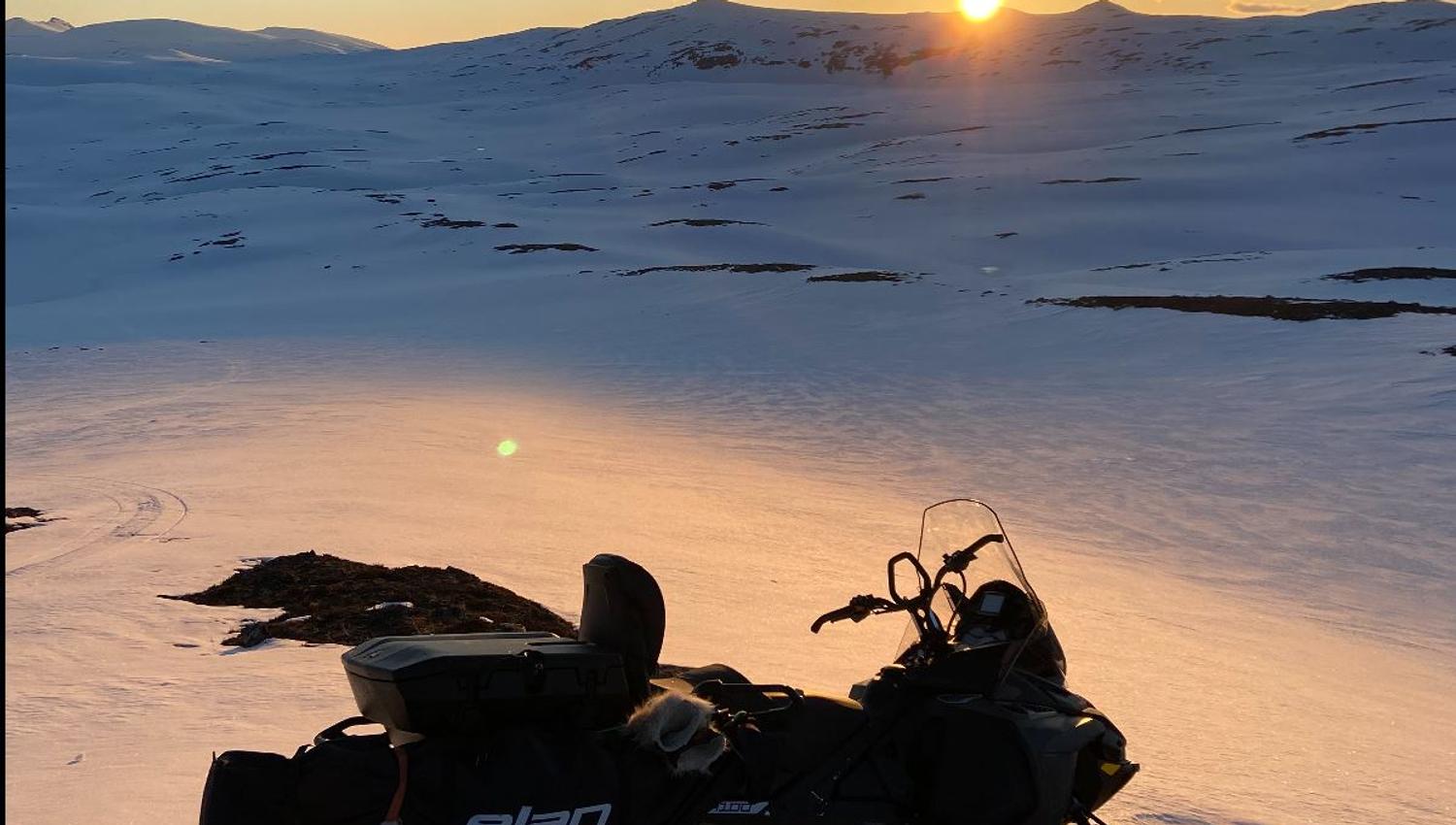 A snowmobile on the mountain with the sun just rising above the peaks