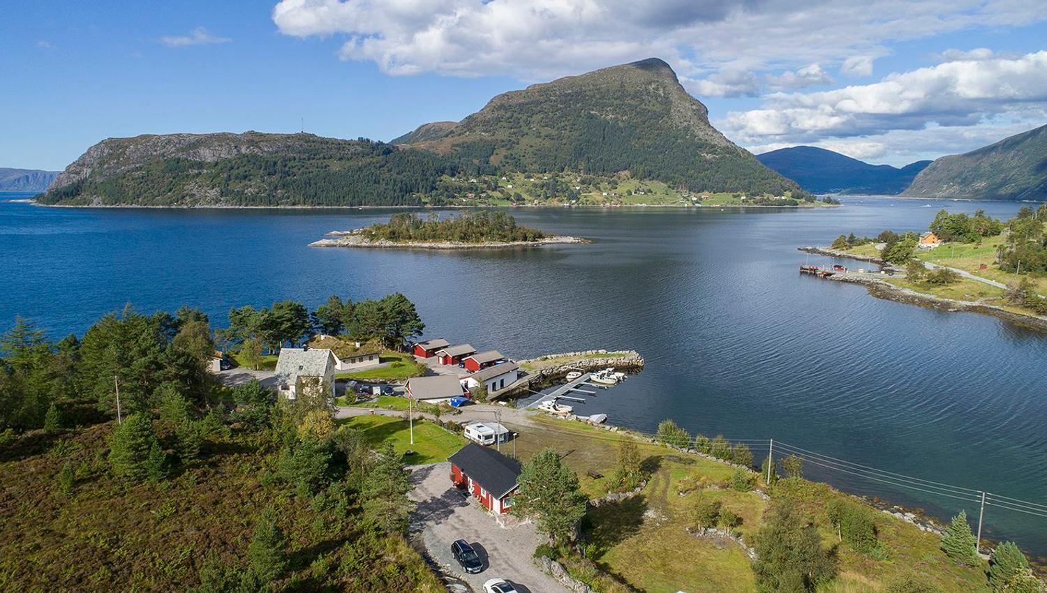 A small waterfront settlement with houses and a marina on a blue lake, backed by forested mountains under clouds..