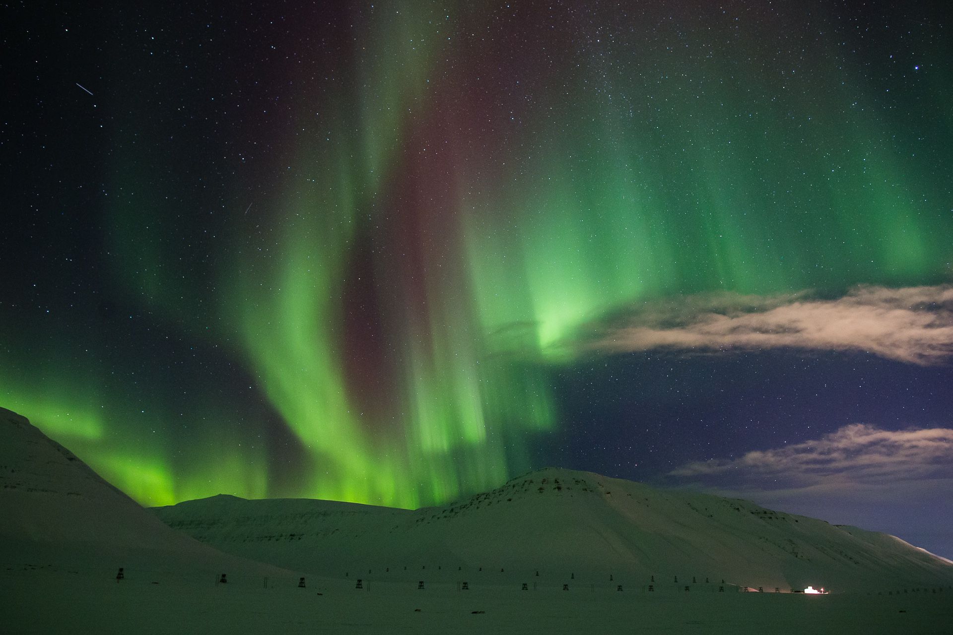 A mountainous landscape in the foreground with northern lights in the skies in the background