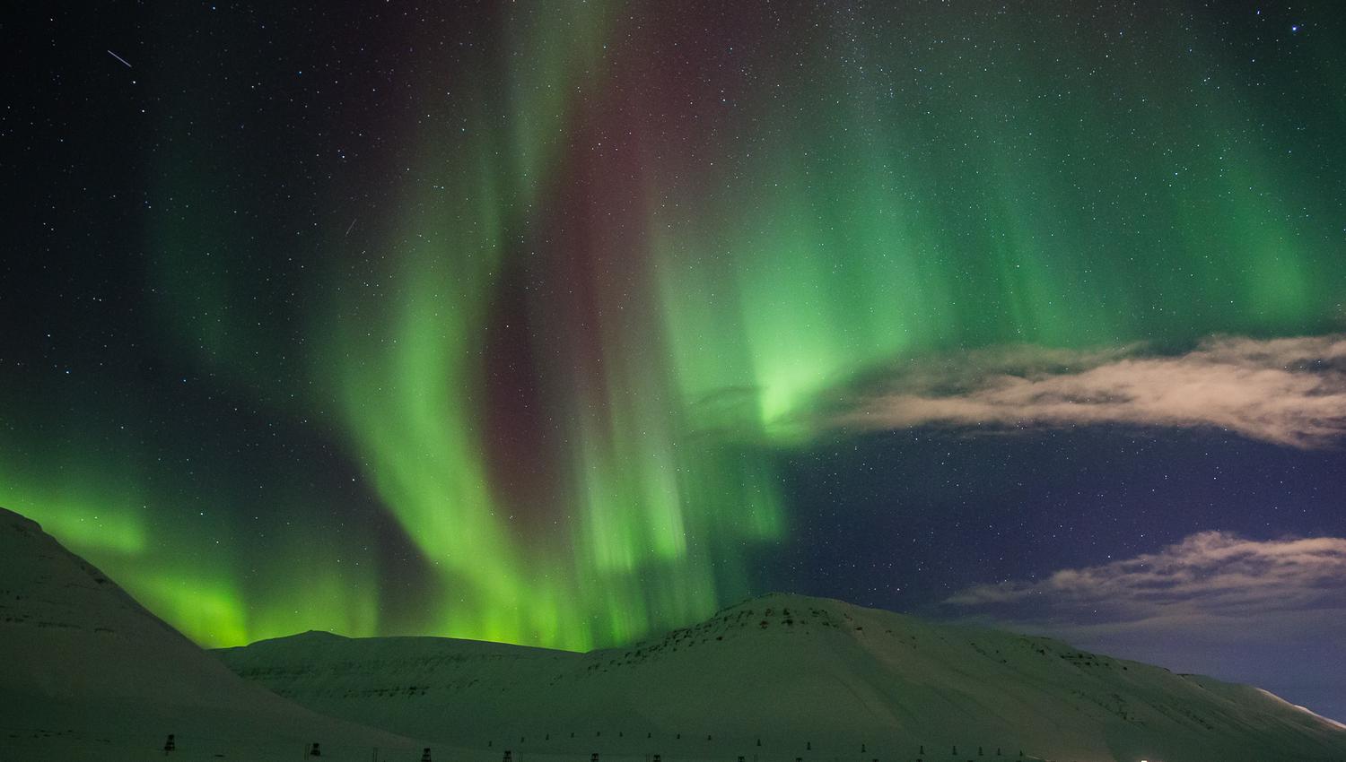 A mountainous landscape in the foreground with northern lights in the skies in the background