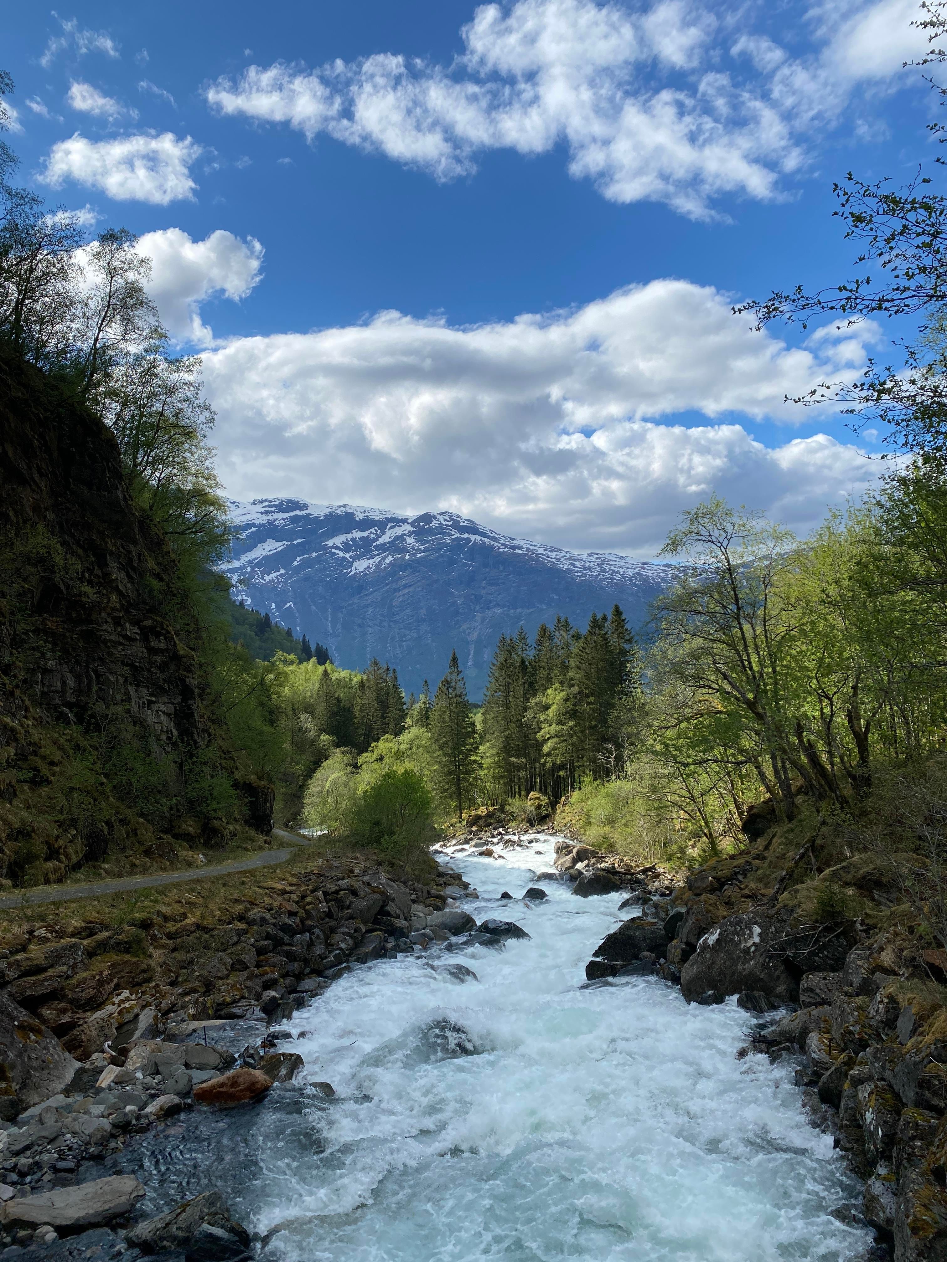Rushing river flowing through Elvedalen valley at Lofthus with snow-capped mountains in the background.