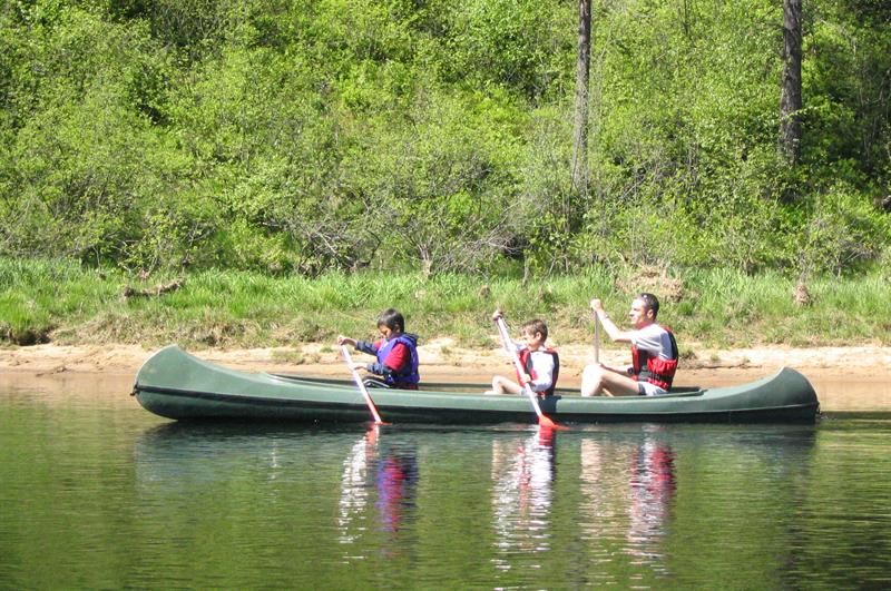 One adult and two children paddling in a green canoe