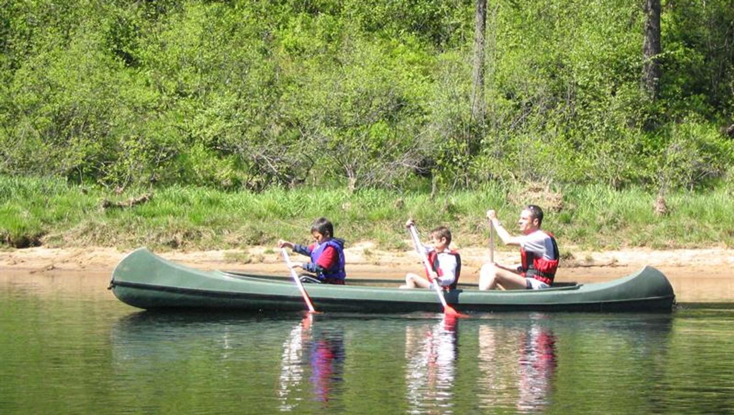 One adult and two children paddling in a green canoe