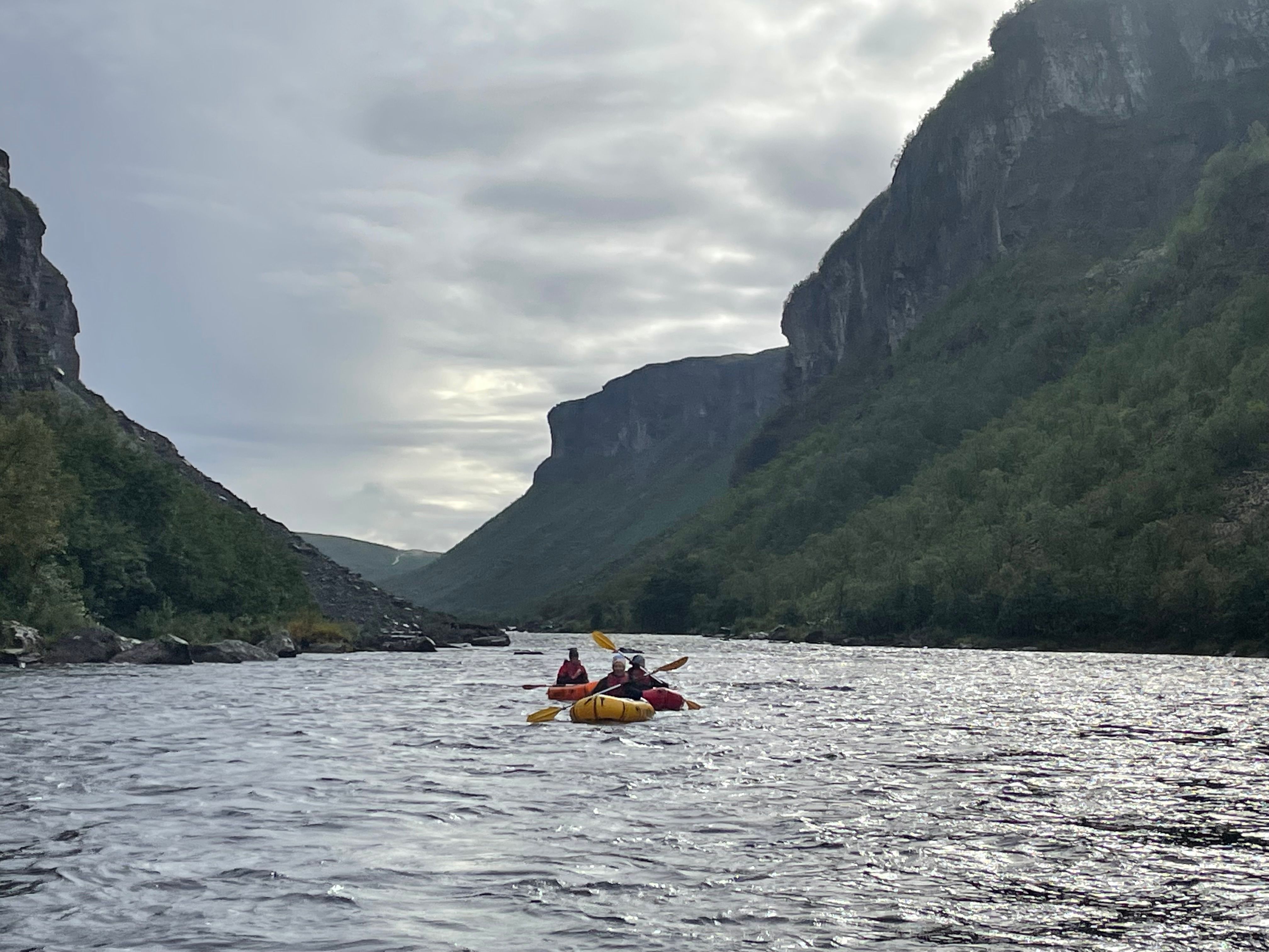 Trois personnes en kayak sur une rivière entourée de falaises verdoyantes.