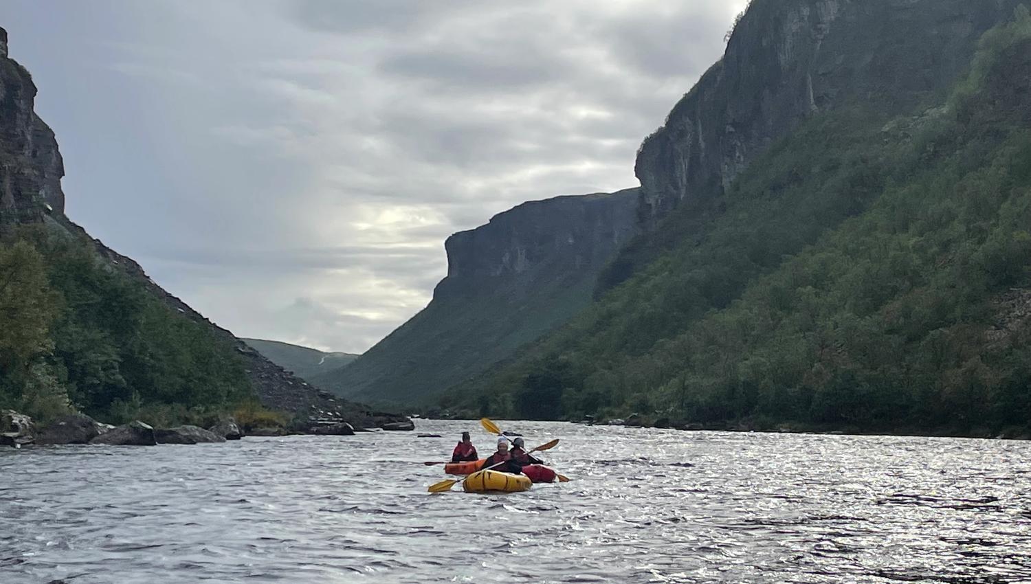 Trois personnes en kayak sur une rivière entourée de falaises verdoyantes.