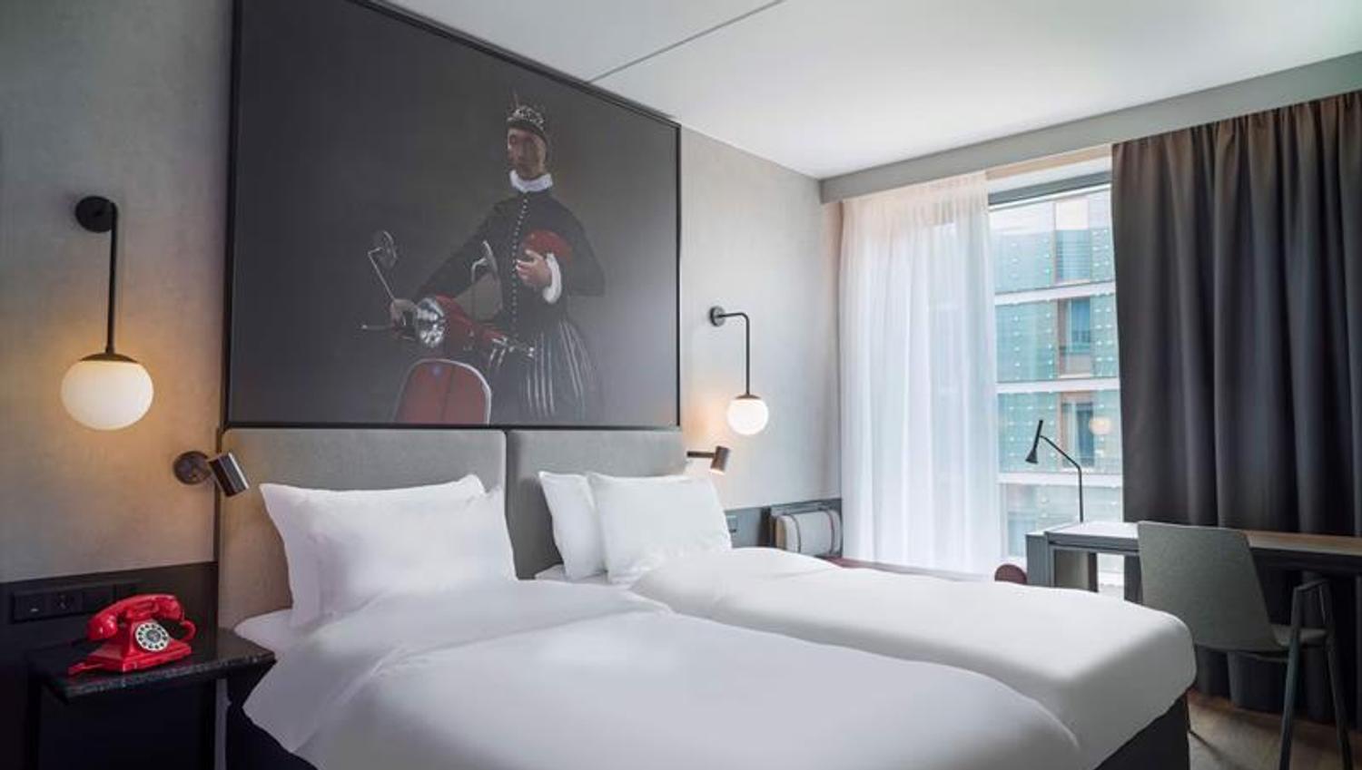 Interior of standard room with double bed, blackout curtains and a large painting above the bed