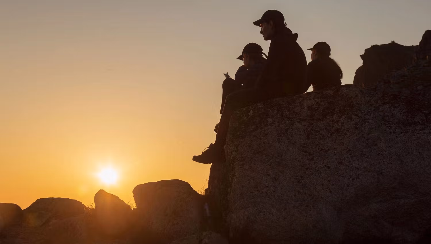 A group sitting on a rock and watching the midnight sun