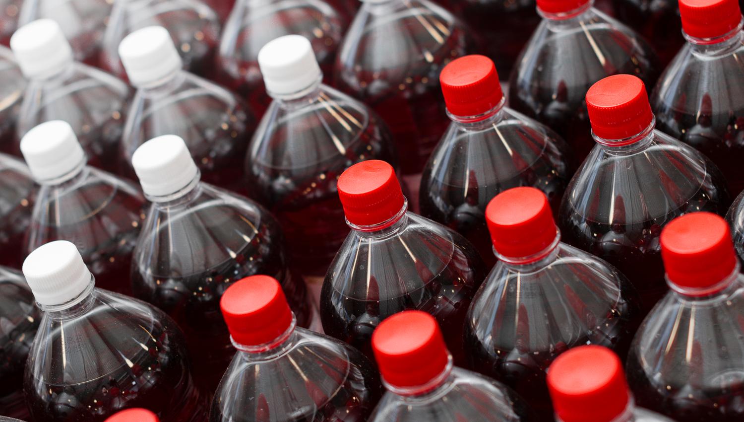Mange plastflasker med mørk brus, toppet med røde og hvite korker, ordnet i rader.