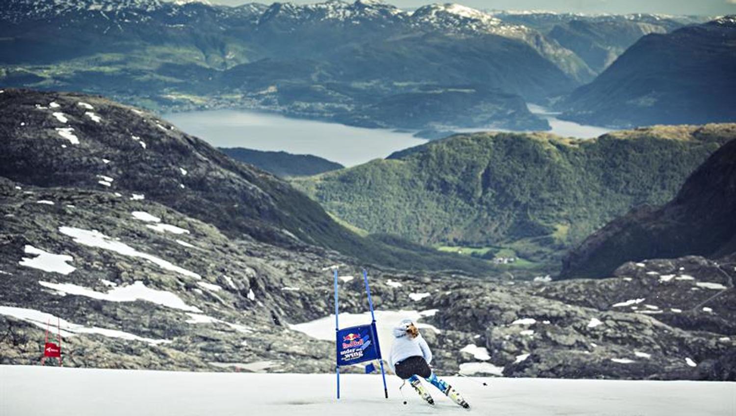 Alpinist køyrer ned sommarsnøen på Fonna Glacier Ski Resort med Hardangerfjorden i bakgrunnen.