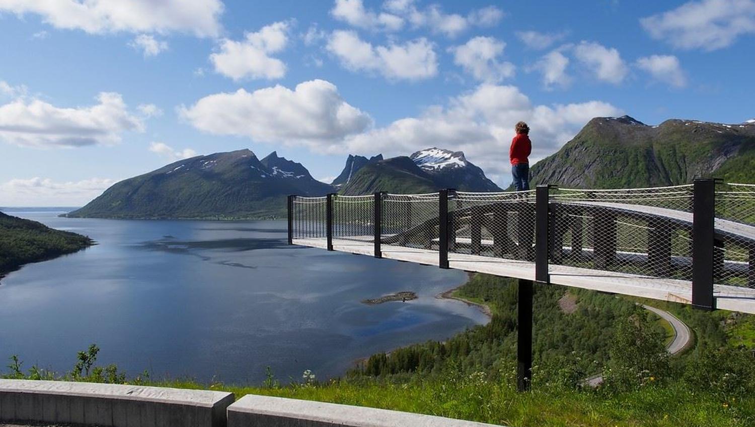 En besøkende på en utsiktsplattform med utsikt over fjord og fjell på Senja