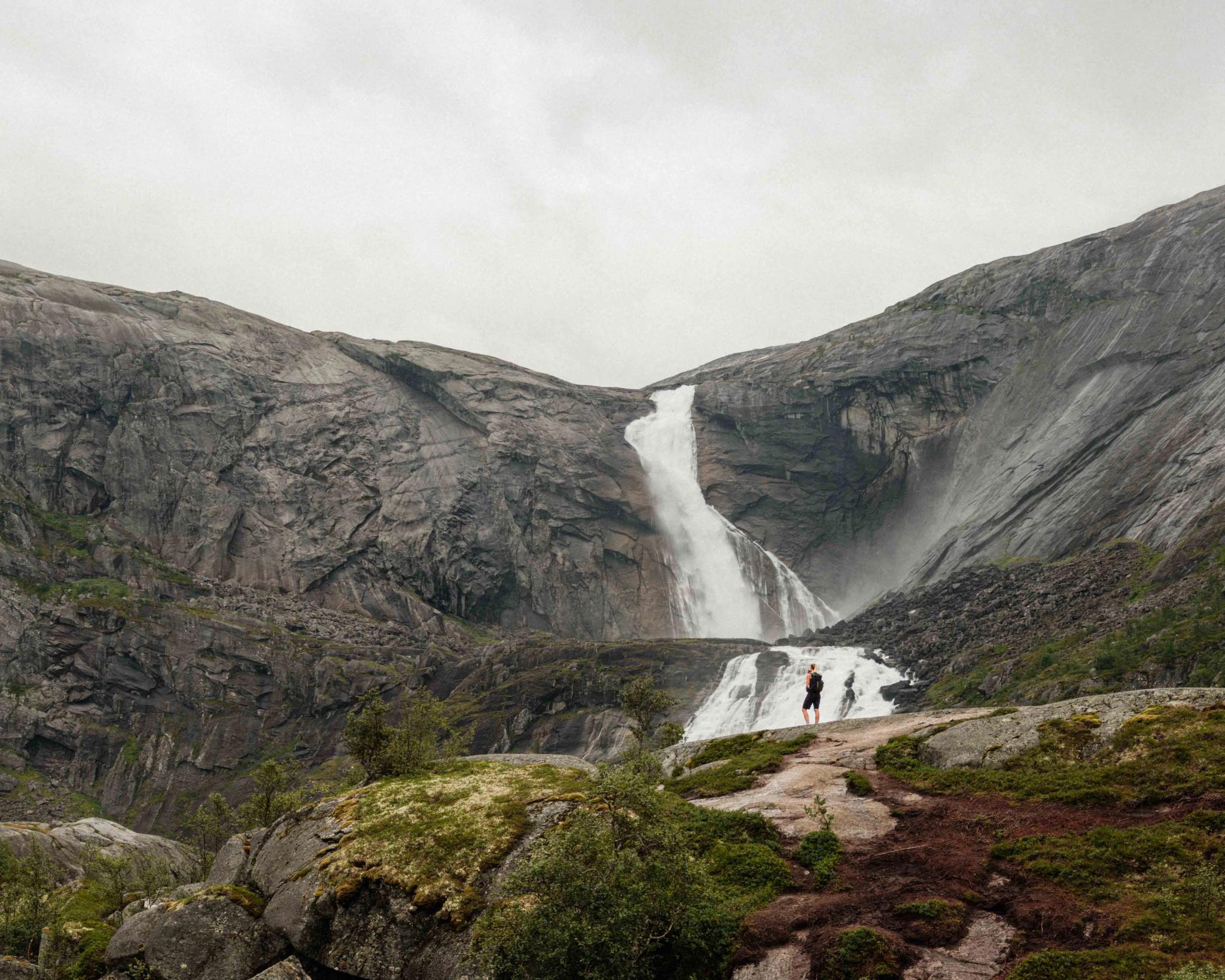 Two hikers admire the powerful Søtefossen waterfall in Husedalen, surrounded by dramatic cliffs and roaring water.
