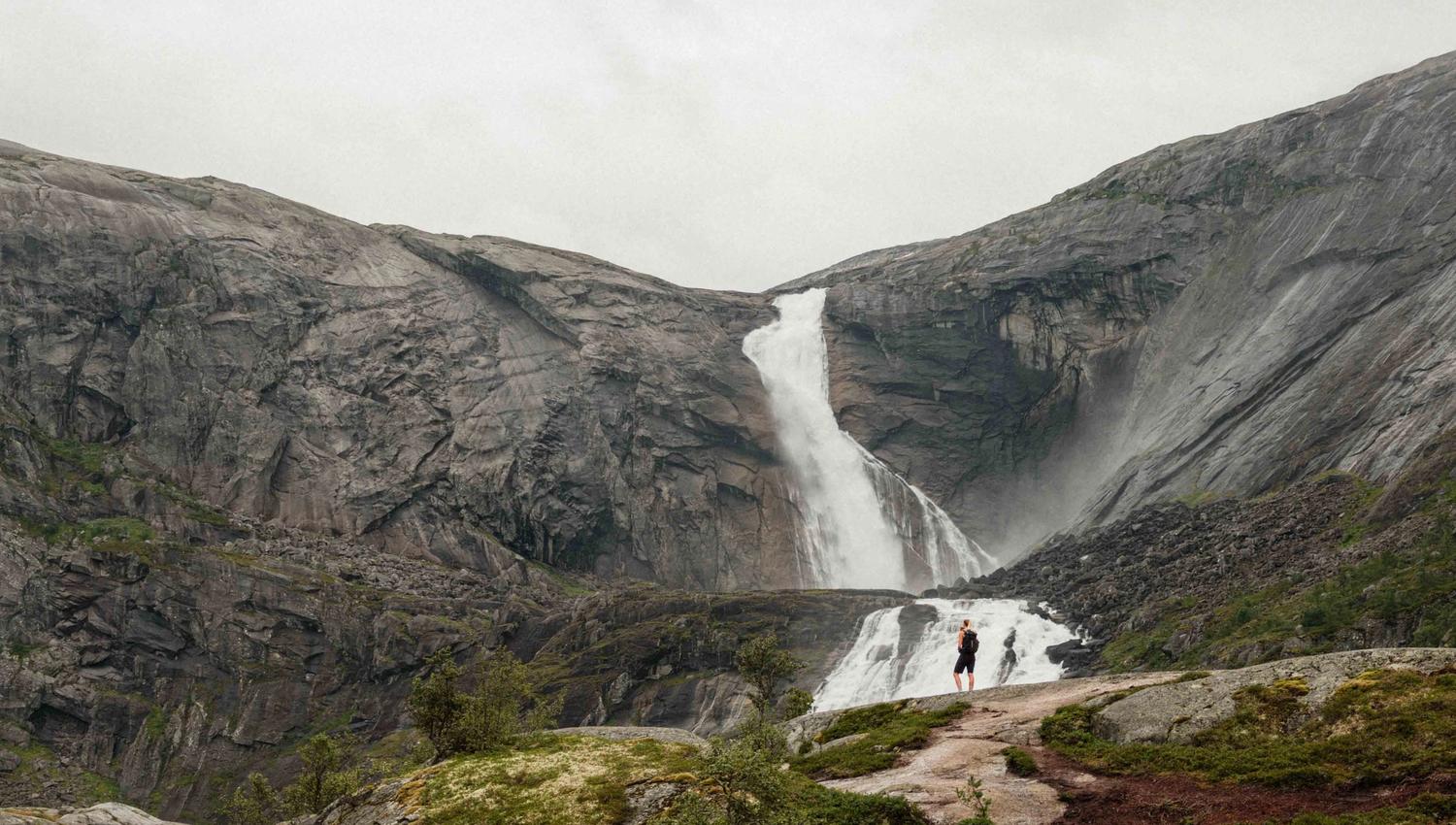 Two hikers admire the powerful Søtefossen waterfall in Husedalen, surrounded by dramatic cliffs and roaring water.