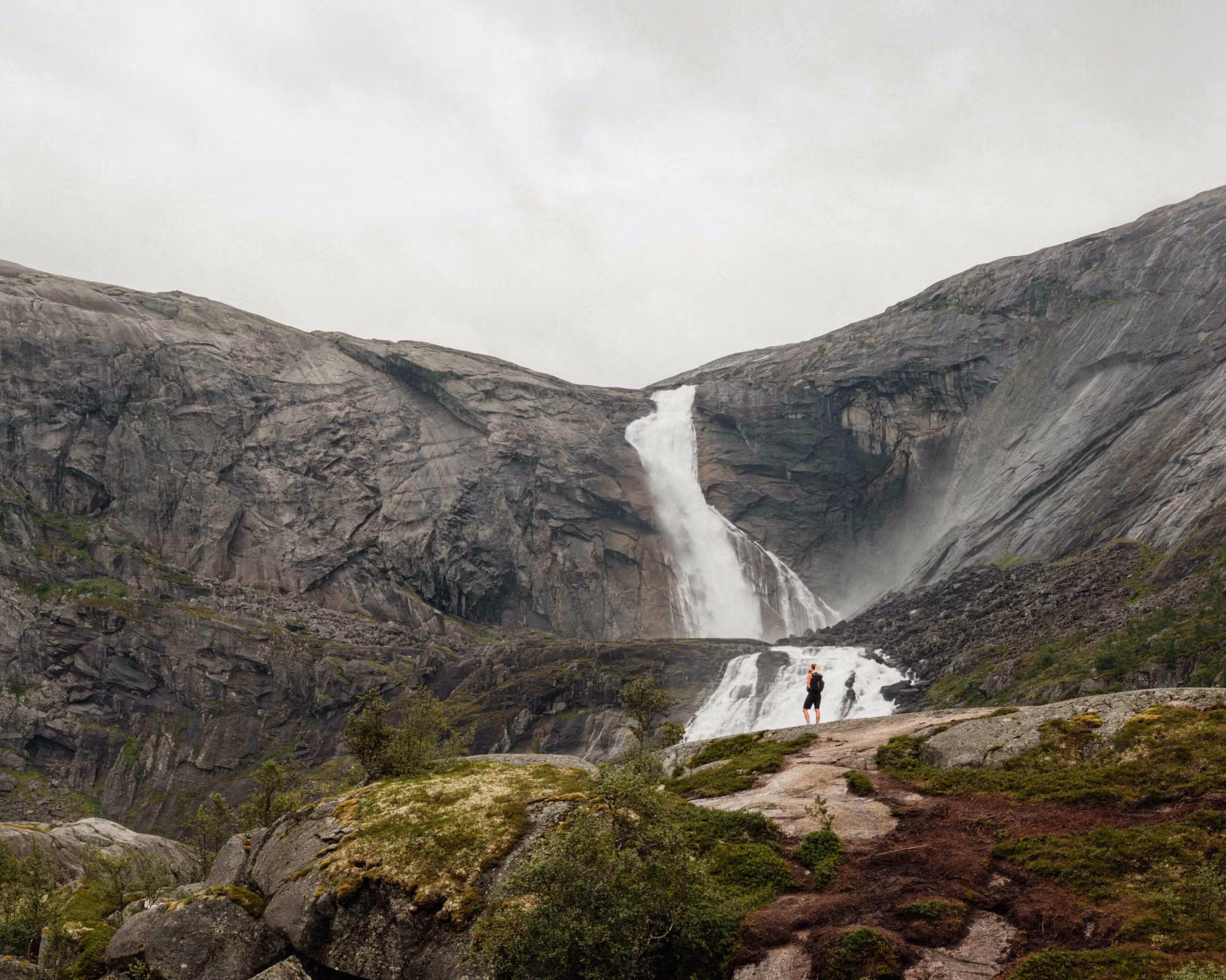 Two hikers admire the powerful Søtefossen waterfall in Husedalen, surrounded by dramatic cliffs and roaring water.