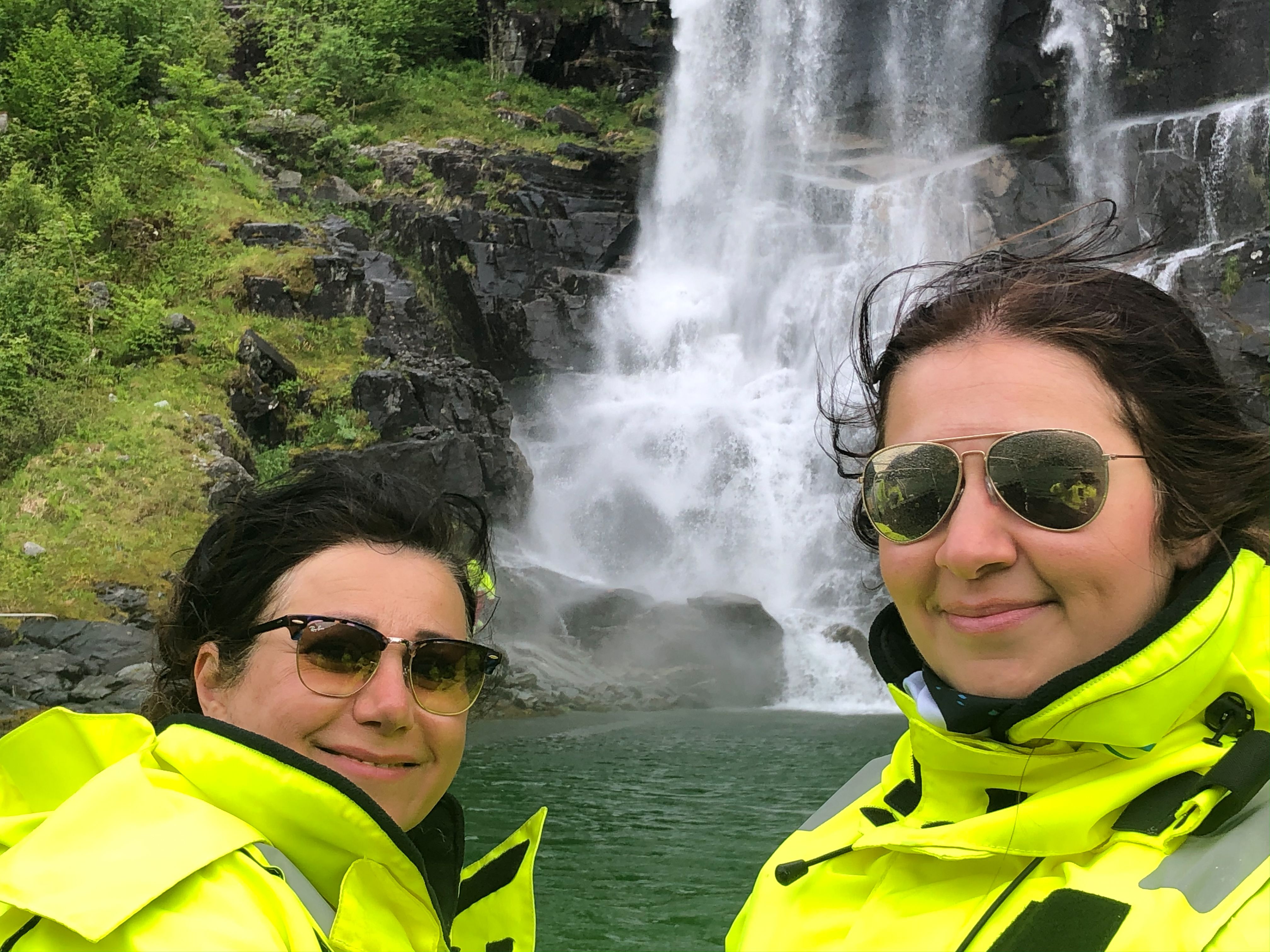 Two tourists in yellow suits enjoying the sight of a roaring waterfall on a RIB safari in Hardanger.