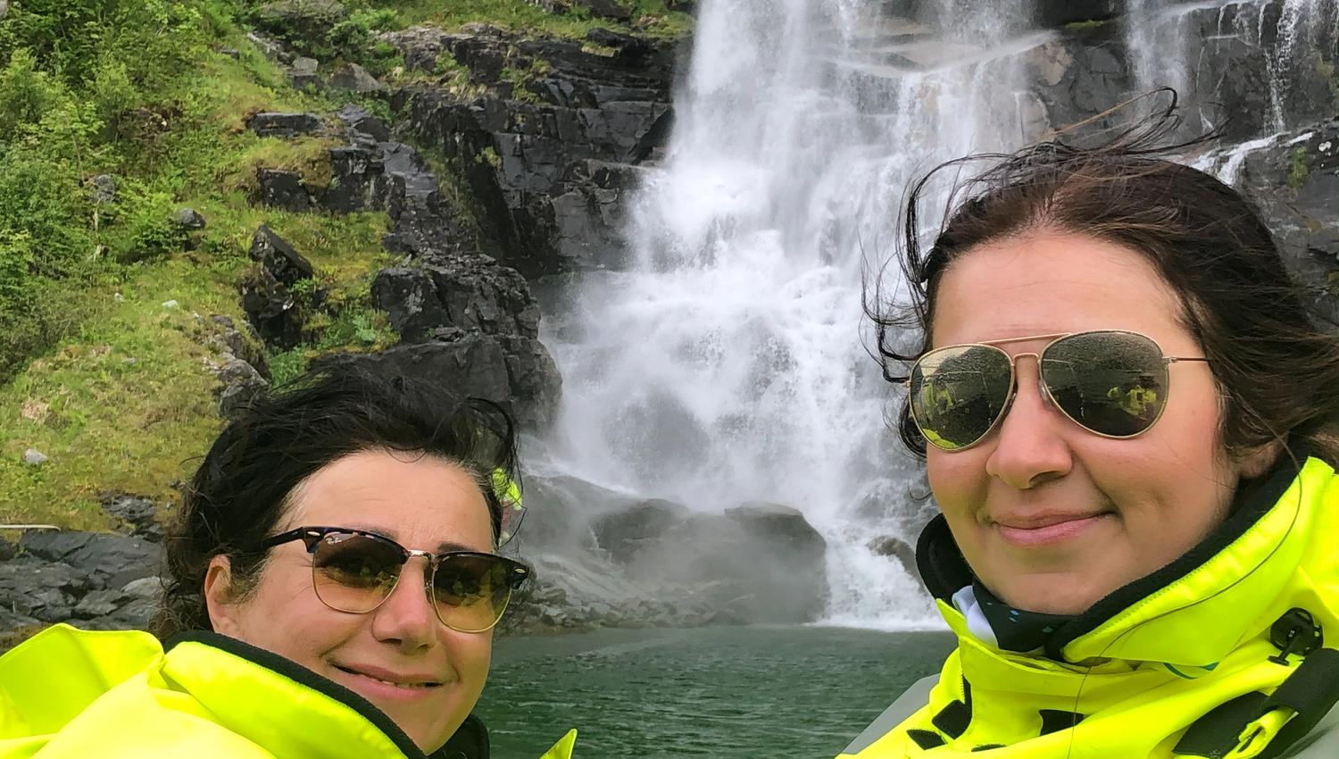 Two tourists in yellow suits enjoying the sight of a roaring waterfall on a RIB safari in Hardanger.