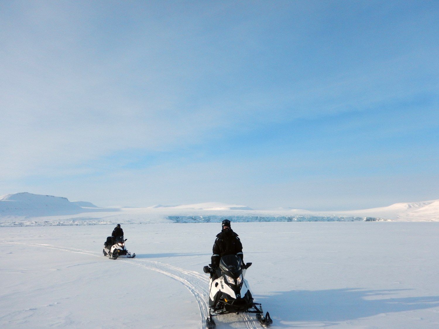 Two people driving on snowmobiles 