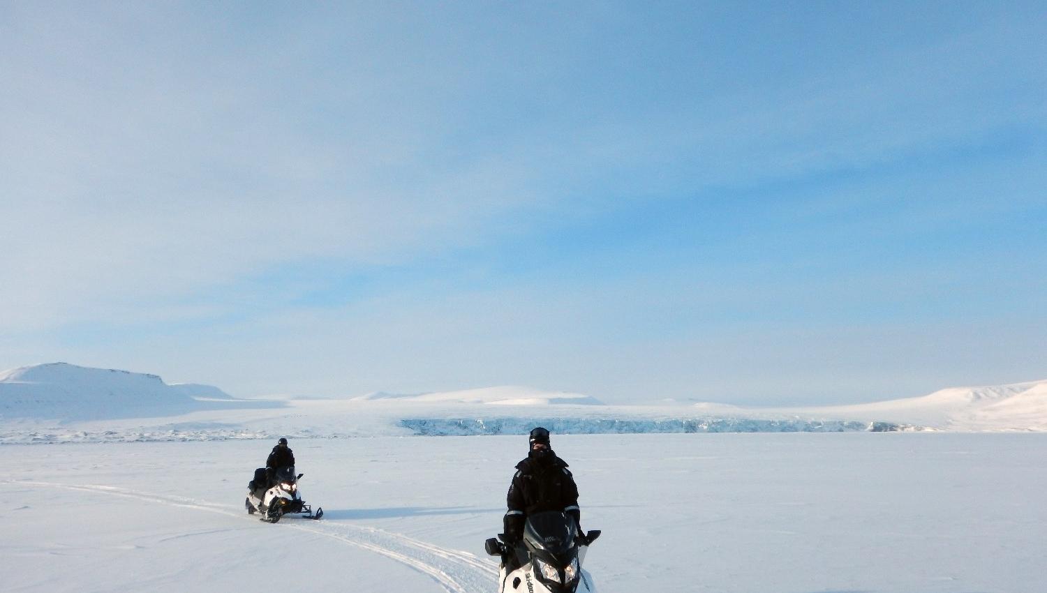 Two people driving on snowmobiles