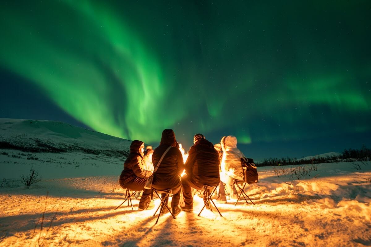 Guests cozy around a fire while the Northern Lights dance overhead