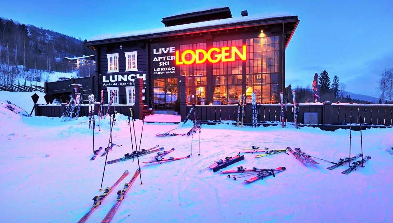 Opplyst trelodge i snødekt fjellområde i skumringen, med ski og staver lagt utover snøen foran bygget..