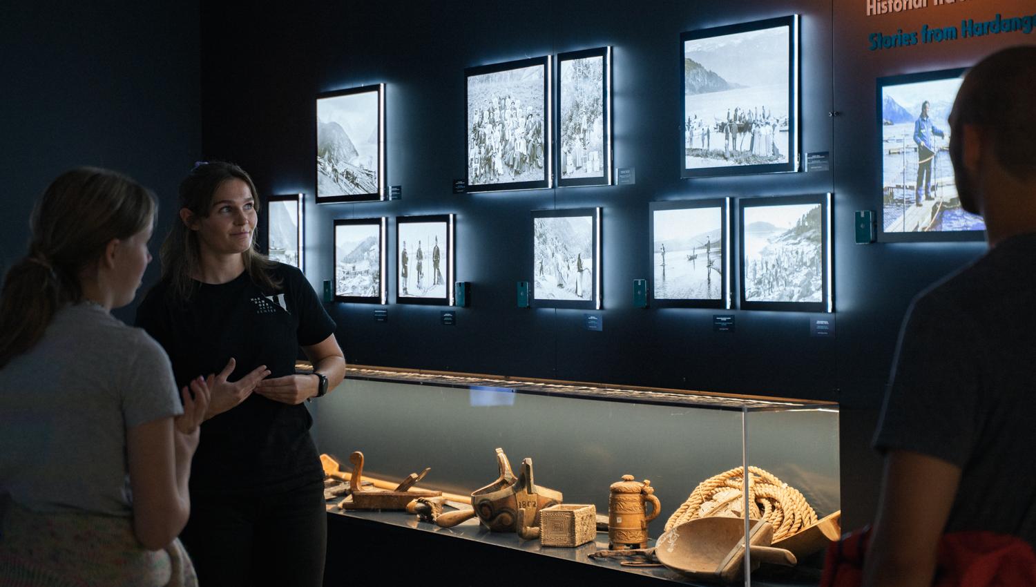 Exhibition wall with historical photos and traditional Hardanger artefacts in the “This is where we live” display.