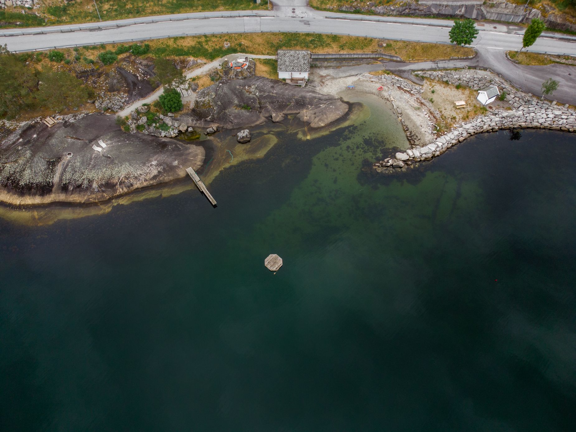 A drone shot of the Kråkeskarvet beach, showing the swim platform in the fjord, diving board, wardrobe building and the beach area.